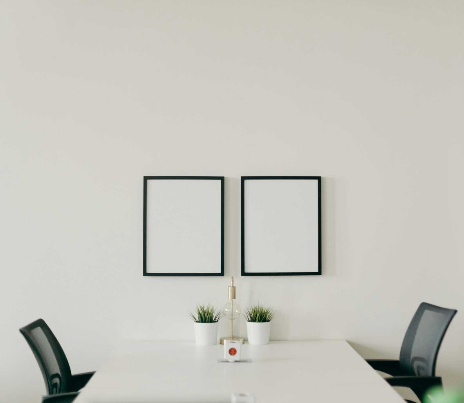 Elegant minimalist home office with white desk, black chairs, and decorative plants, emphasizing simplicity.