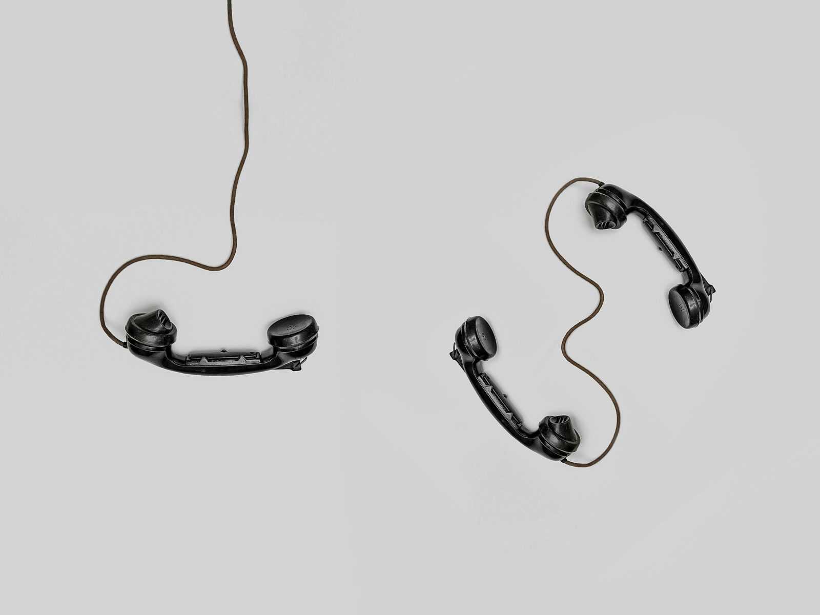 Two vintage black telephone handsets connected by cords on gray background.